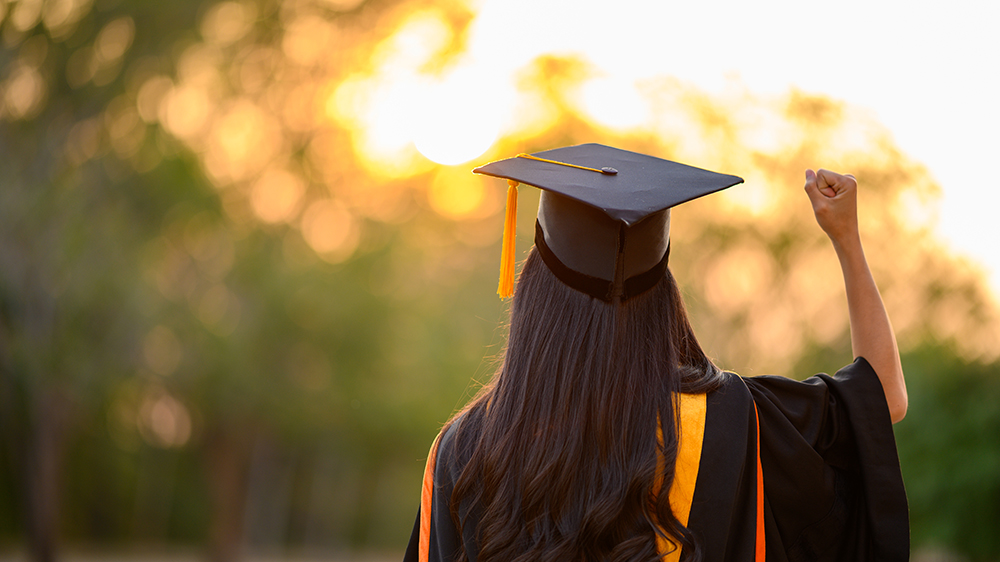 View from behind of female student in graduate robes, making a victory fist.