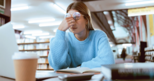 Stressed or tired student rubs her eyes while seated in a library