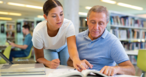 Young person pointing something out in a book to an older person