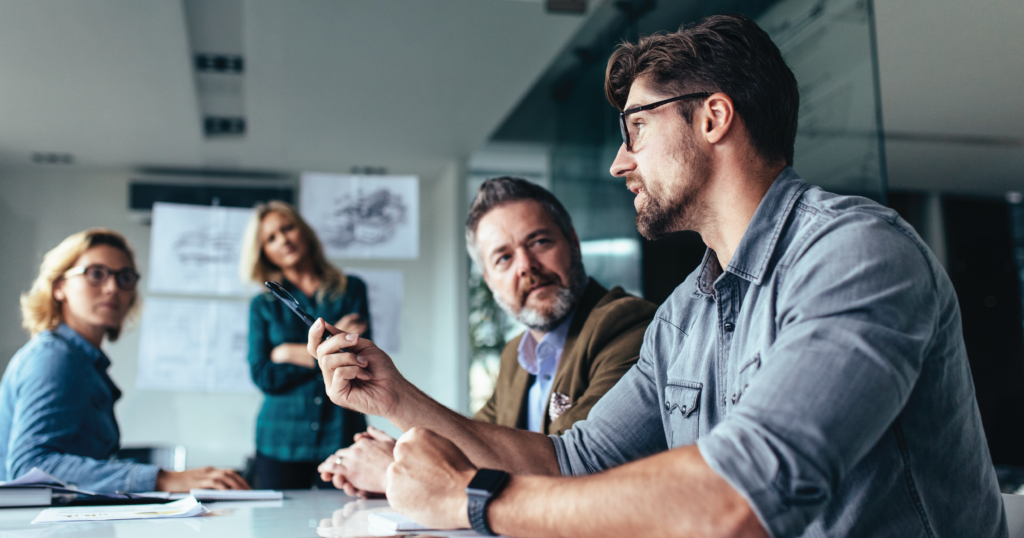 Group of adults sitting in a conference room, engaged in active discussion. The graphic represents the collaborative nature of the client-vendor relationship.